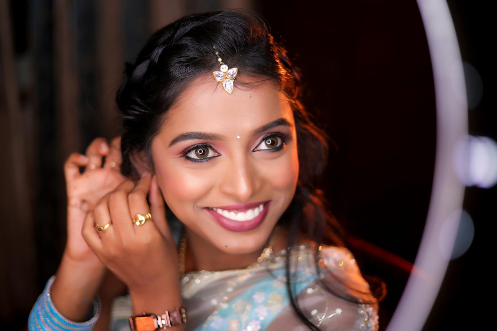 Smiling woman in traditional attire puts on earrings with mirror reflection, highlighting elegance.