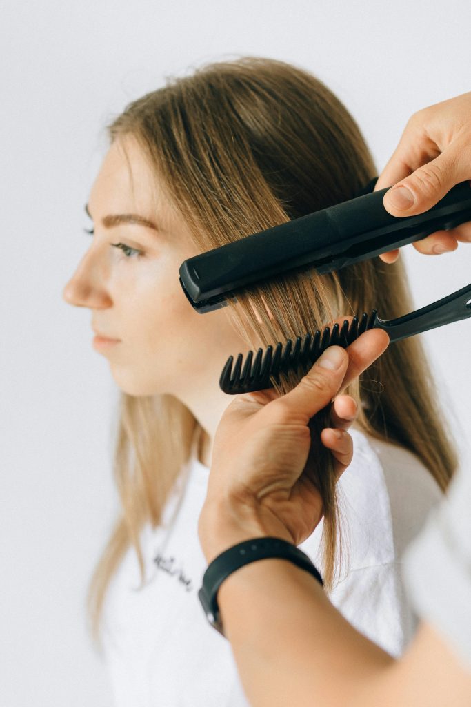 Close-up of a woman getting her hair styled with a flat iron and comb.