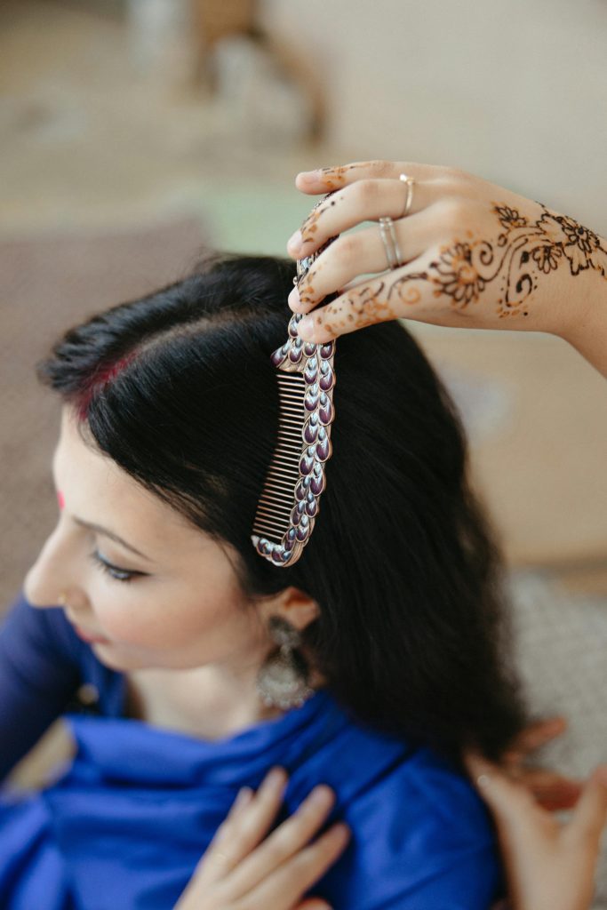 A woman with henna hands combs another's long hair in a cultural setting.